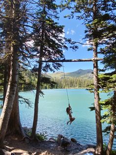 a person hanging from a rope in the air over a body of water surrounded by trees