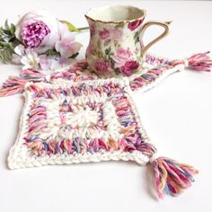 a crocheted square with tassels and a coffee cup sitting on it