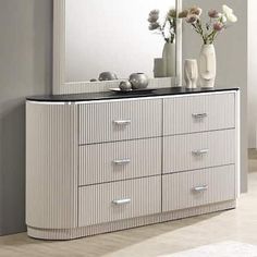 a white dresser with flowers and vases on it in front of a large mirror