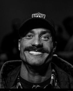 a black and white photo of a man with a hat on smiling at the camera