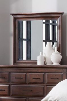 a bedroom scene with focus on the dresser and large mirror in the middle, along with white vases