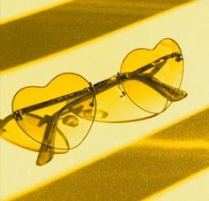 a pair of heart shaped glasses sitting on top of a yellow surface with the sun shining through it