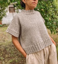 an older woman standing in front of a tree with her hands on her hips and looking off to the side