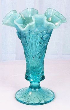 a blue glass vase sitting on top of a white table next to a curtained window