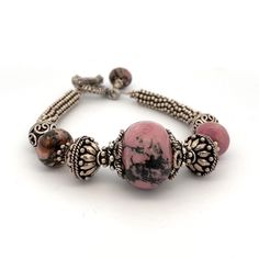 "Handmade Pink and Black Rhodonite Gemstones and Silver Beaded Bracelet  925 Solid Sterling Silver with a Toggle Clasp 8\" bracelet- Fits a larger wrist Beautiful and Unique Toggle Bracelet! Metal Content: 925 Sterling Silver Clasp: Toggle Clasp Measurements Length:  8\"  Width:  13/16\" (20mm) Weight: 51.52 Grams Marked: none Very Good pre-owned Condition Each piece is thoroughly examined and refinished as needed by our professional jewelers, tested to guarantee metal content,  graded by our in-house GIA (Gemological Institute of America) Graduate Gemologist, and inspected for quality before being carefully packaged and promptly shipped. Thank you for taking the time to shop with us! We have hundreds of more listings, with more being added every week! From necklaces to bracelets, the clas Handmade Beaded Bracelets In Sterling Silver With Fusion Style, Fusion Style Jewelry With Silver Beads, Artisan Silver Beaded Bracelets With Gemstones, Artisan Hand-strung Sterling Silver Beaded Bracelets, Artisan Beaded Bracelets With Natural Stones In Sterling Silver, Artisan Sterling Silver Beaded Bracelet With Natural Stones, Artisan Sterling Silver Bracelets With Round Beads, Artisan Gemstone Beads Bracelets, Artisan Hand-strung Sterling Silver Bracelets