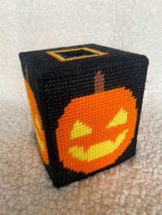 an orange and black beaded halloween cube on a white surface with a pumpkin in the middle