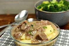 a glass bowl filled with beef and gravy on top of a checkered table cloth