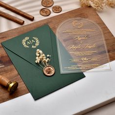 a green and gold wedding card on top of a wooden table next to some coins