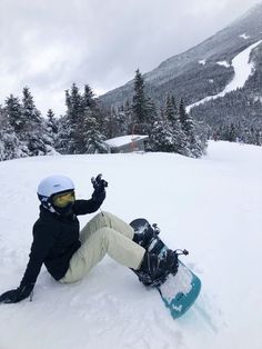 a person sitting in the snow with a snowboard on their feet and one hand up