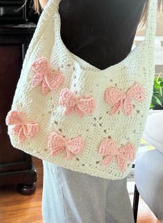 a crocheted purse with pink bows on the front and bottom, sitting on top of a mannequin