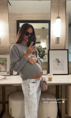 a pregnant woman taking a selfie in front of a mirror with her cell phone