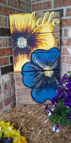 a wooden sign with flowers painted on it in front of a brick wall and some hay