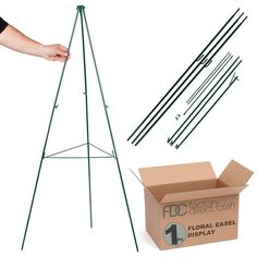 a green easel stands next to a cardboard box and several black rods on a white background