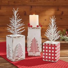 three white christmas decorations sitting on top of a red place mat next to a lit candle