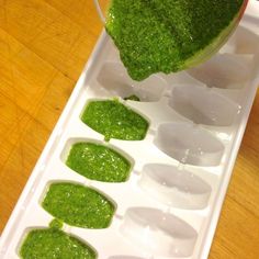 a person pouring green liquid into an ice tray with hearts on it and small pieces of broccoli in the middle