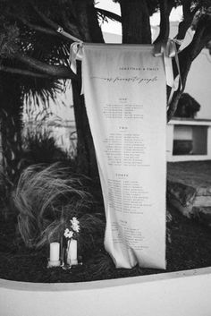 a wedding ceremony sign hanging from a tree in front of a house with candles and flowers