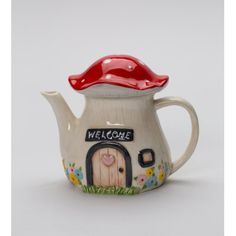 a ceramic teapot with a welcome sign on the front and a red cap on top