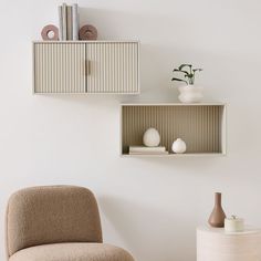 two shelves on the wall with vases, books and other items in them next to a chair