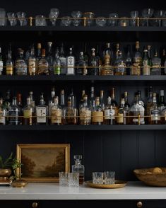 an assortment of liquor bottles and glasses on a shelf in a room with black walls