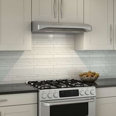 a bowl of fruit sitting on top of a stove in a kitchen next to white cabinets