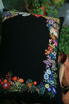 a black pillow with colorful flowers on it sitting in front of some potted plants