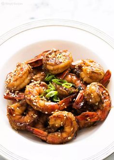 a white plate topped with cooked shrimp and sesame seed sprinkled on top of it