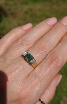 a woman's hand holding a ring with an emerald and diamond set in it