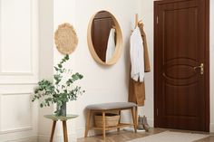 an entryway with a bench, coat rack and mirror on the wall next to a potted plant