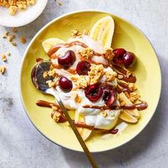 an ice cream sundae with cherries and nuts on a yellow plate next to a spoon