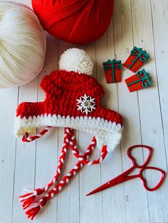 red and white crocheted hat next to yarn, scissors and other crafting supplies