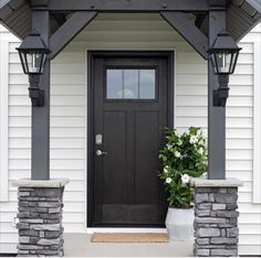 a black front door on a white house with stone steps and planters in the foreground