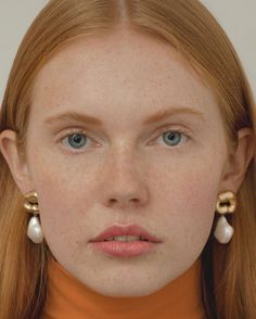 a woman with freckled hair and blue eyes is wearing gold earrings