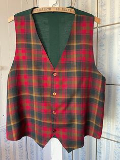 This striking vest is made from a lightweight wool blend in classic tartan in red, dark green and harvest gold. It buttons in the front and is partially lined with dark red silky lining. The back is made of a fine knit in dark green. The measurements, taken with the vest lying flat, are: shoulder to shoulder, 13 1/2 inches; armpit to armpit, 20 1/2 inches; length 25 1/2 inches (front) and 22 inches (back); bottom edge, 20 inches. Please note that the back has a few small holes; otherwise, the vest is in very good condition. Classic Red Vest For Fall, Classic Green Vest For Winter, Classic Green Winter Vest, Classic Plaid Vest For Fall, Classic Plaid Vest, Classic Plaid Sleeveless Vest, Classic Sleeveless Plaid Vest, Plaid Vest For Fall, Plaid Sleeveless Vest For Fall