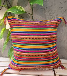 a multicolored pillow sitting on top of a wooden bench next to a plant