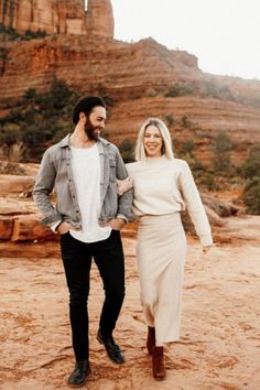 a man and woman are walking in the desert with their arms around each other as they hold hands