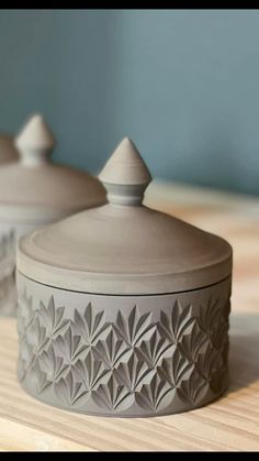 two ceramic containers sitting on top of a wooden table next to each other and one has a lid