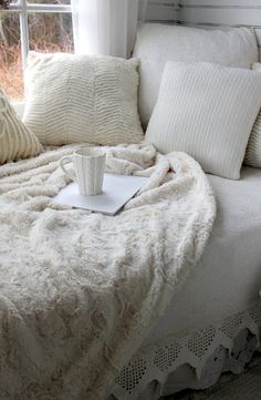 a white couch with pillows and a coffee cup on top of it next to a window