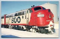 a red and white train traveling down tracks next to a silo in the snow