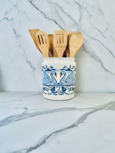 three wooden utensils in a blue and white ceramic jar on marble counter top