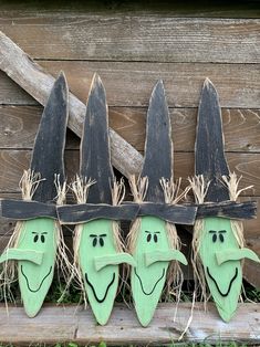 three green faces painted on wooden boards attached to the side of a fence with grass growing in between them