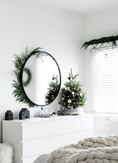 a white bedroom with a round mirror on the wall and christmas decorations in front of it