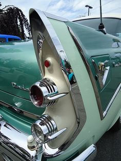 an old green car with chrome rims parked in a parking lot next to other cars