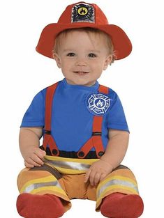 a baby sitting on the ground wearing a fireman's hat and overalls