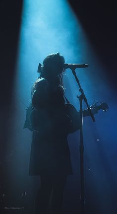 a woman standing in front of a microphone on top of a stage holding a guitar