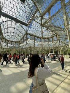 many people are walking around in a large building with glass walls and windows on the ceiling