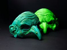 two green alien heads sitting next to each other on a black surface with one looking at the camera