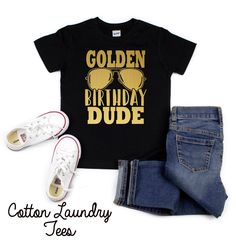 a black shirt that says golden birthday dude with sunglasses on it and jeans are next to the