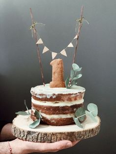 a person holding a cake on top of a tree stump with leaves and bunting