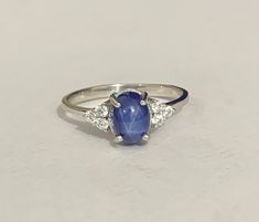 a ring with a blue stone surrounded by three white diamonds on a plain surface,