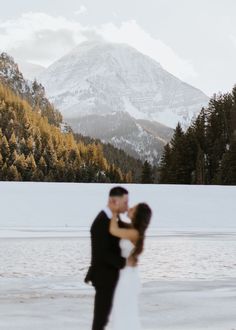 a bride and groom standing in front of a mountain with snow on it's ground